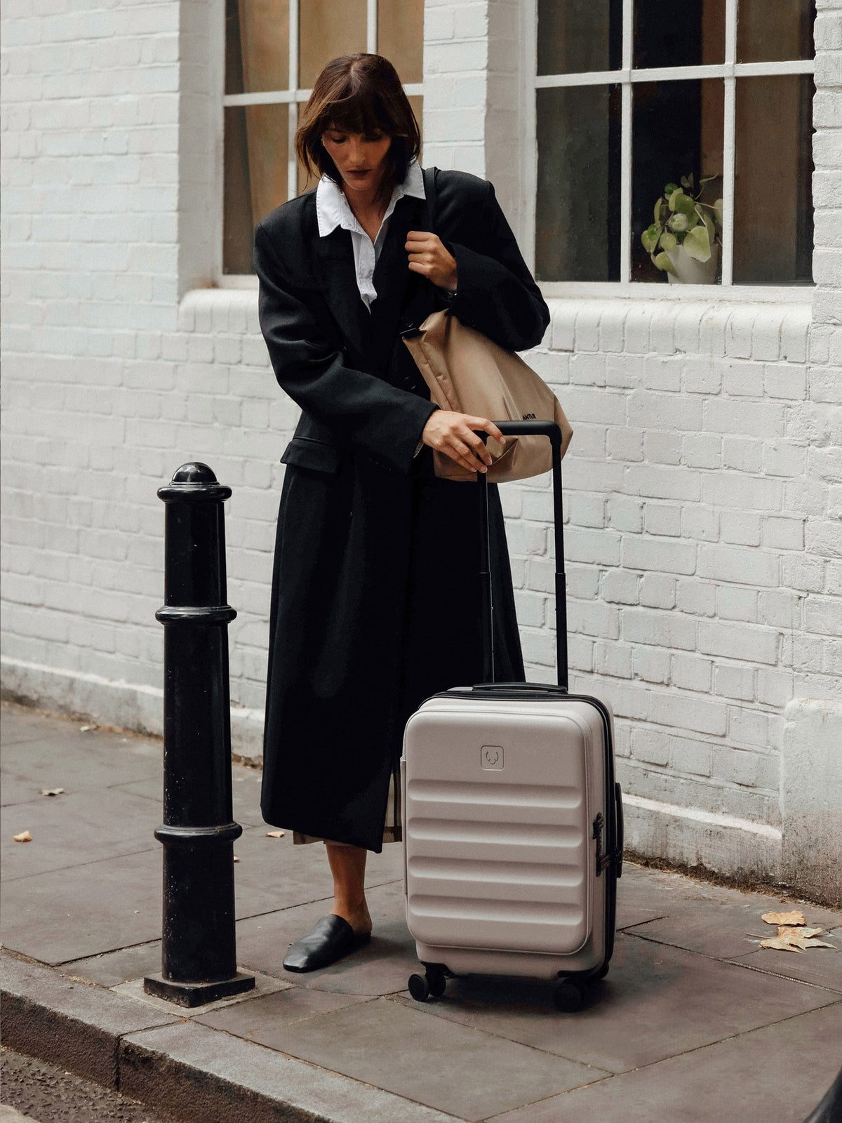 a woman in a long coat and hat pulling a suitcase