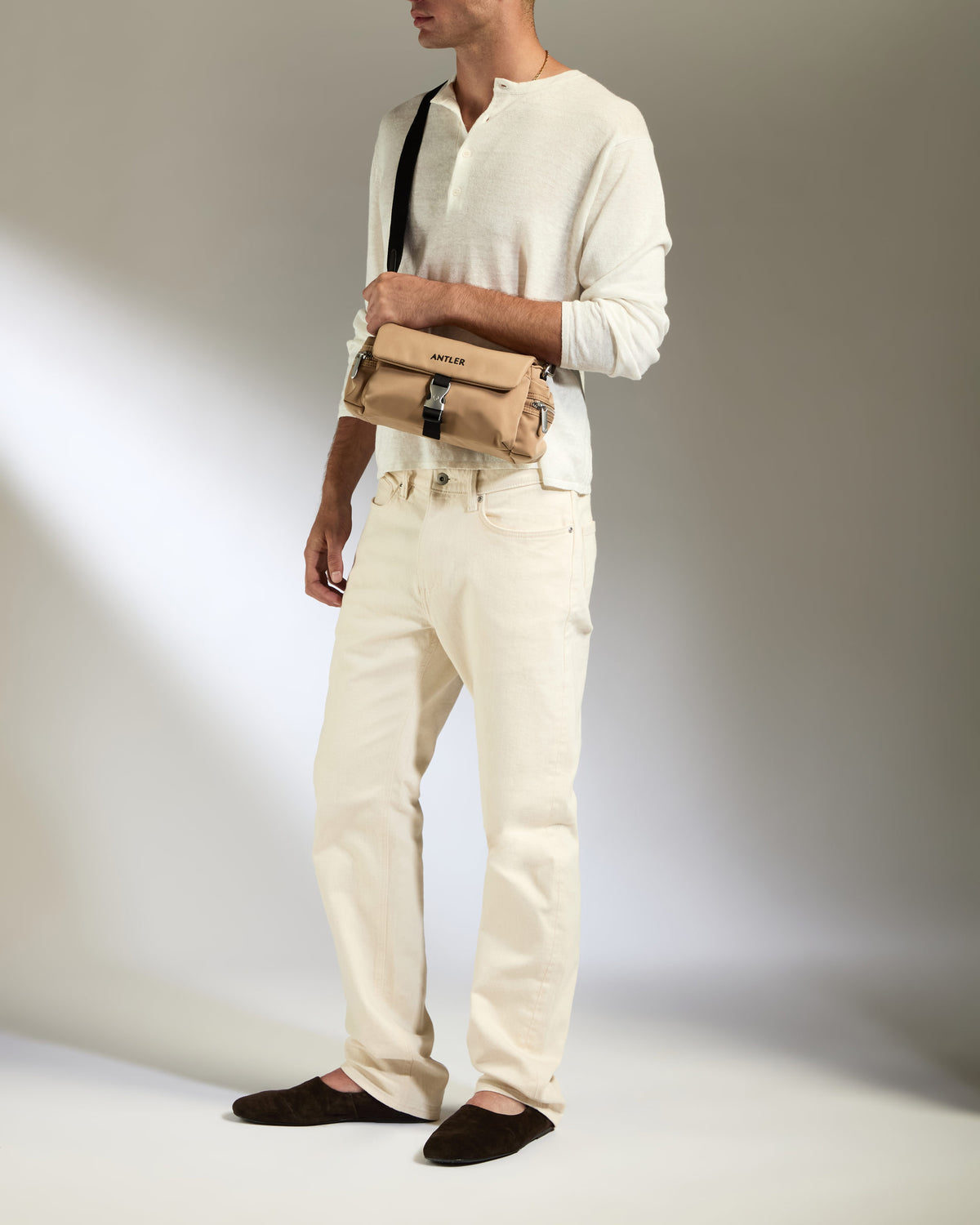 a man in white pants and a white sweater with a tan purse