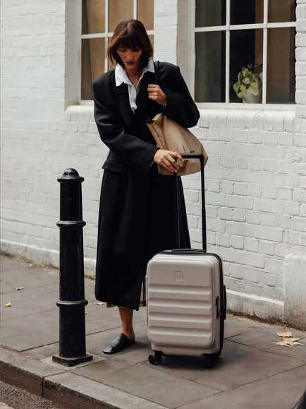 a woman in a long coat and hat pulling a suitcase