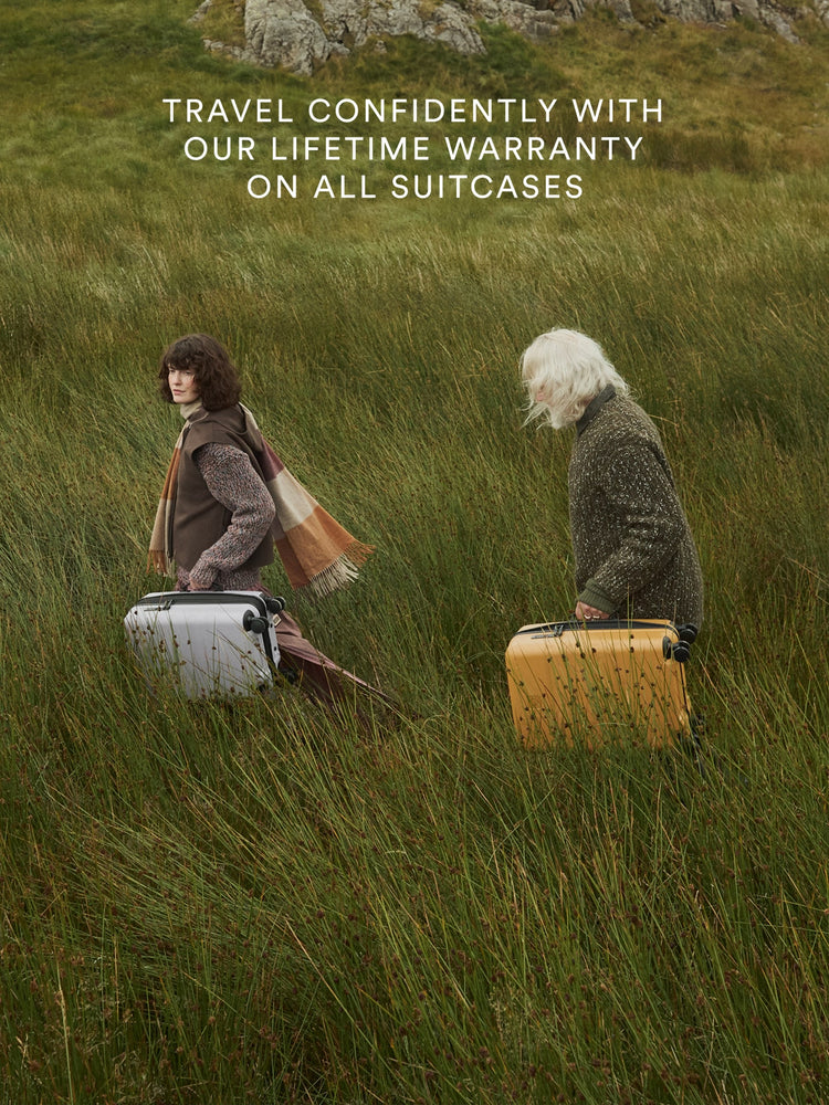 two people walking in tall grass with luggage